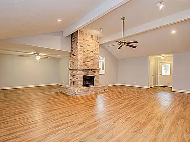 Spacious living room with vaulted ceilings, abundant natural light, and a cozy brick fireplace.