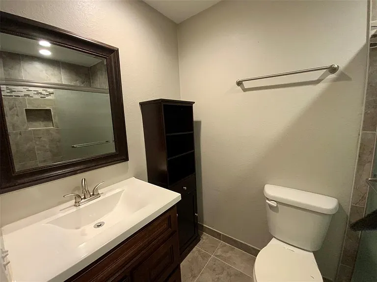 Contemporary bathroom featuring a dark wood-finish vanity with an integrated sink, a framed mirror, and a tile shower with decorative accent tiling and a built-in niche