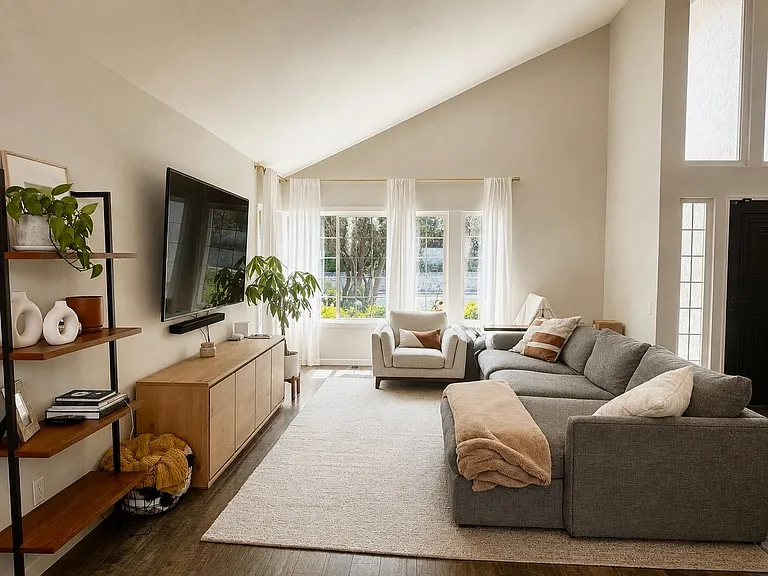 Elegant formal living room featuring soaring vaulted ceilings, expansive picture windows, and abundant natural light. The spacious layout creates a warm and inviting atmosphere while showcasing the home's impressive architectural design and open feel.
