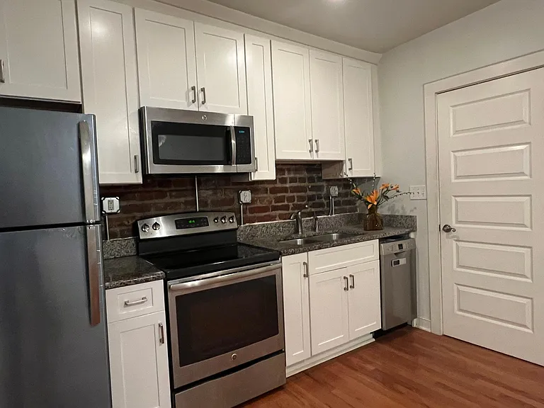 Exposed brick wall, granite counters, new white cabinets and stainless appliances make for a tidy kitchen!