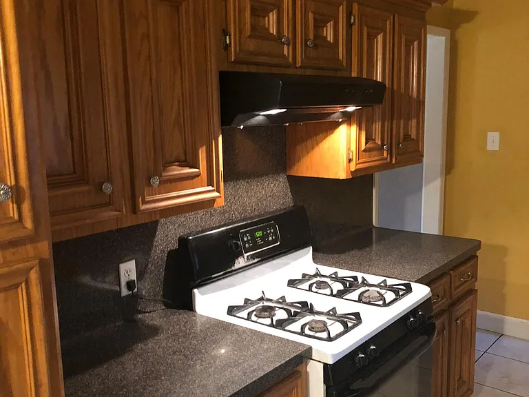 Kitchen features nature toned custom cabinets with silver knobs, range stove, and black counter tops.
