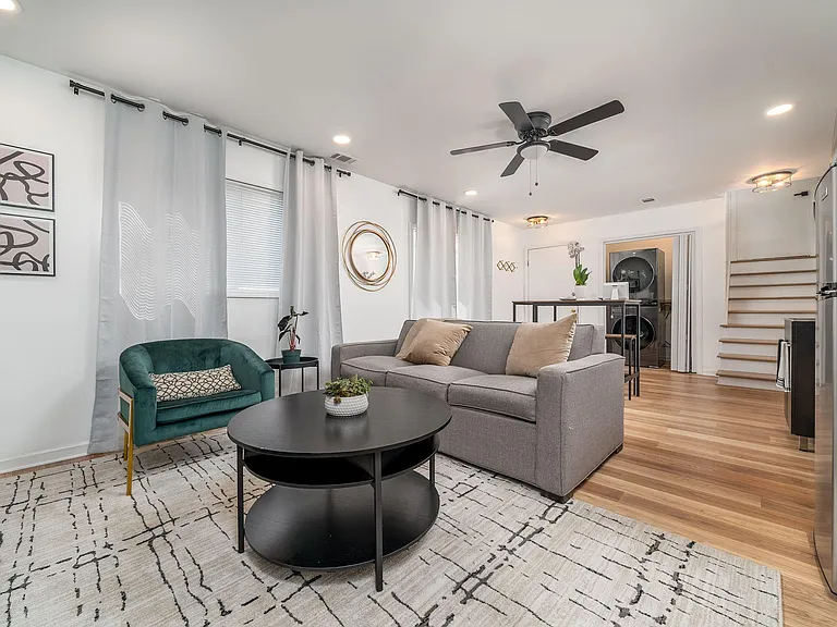 Open living area with comfortable seating, ceiling fan, and window treatments, flowing into the kitchen and nearby laundry.