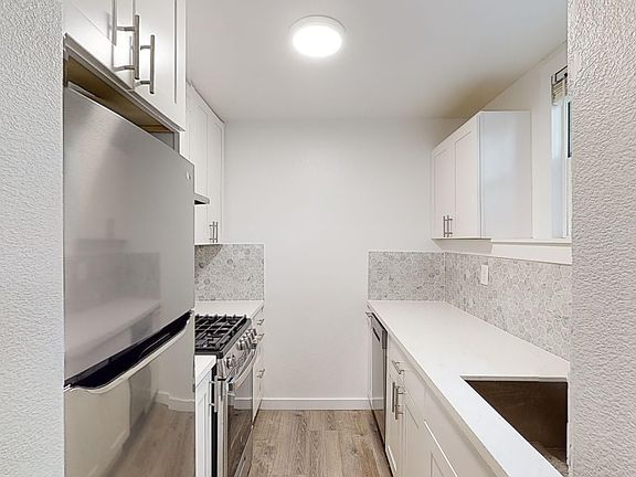 Kitchen with multiple cabinets, refrigerator, stove, range hood, and sink
