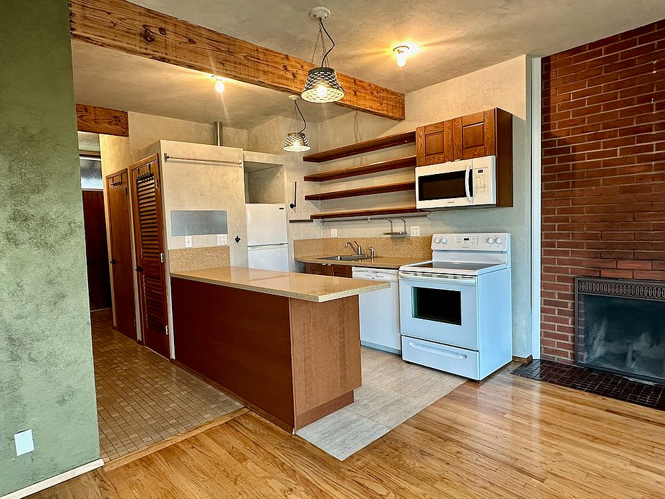 Kitchen with brick fireplace wall to the right, and entrance hallway to the left. Oak and tile floors.