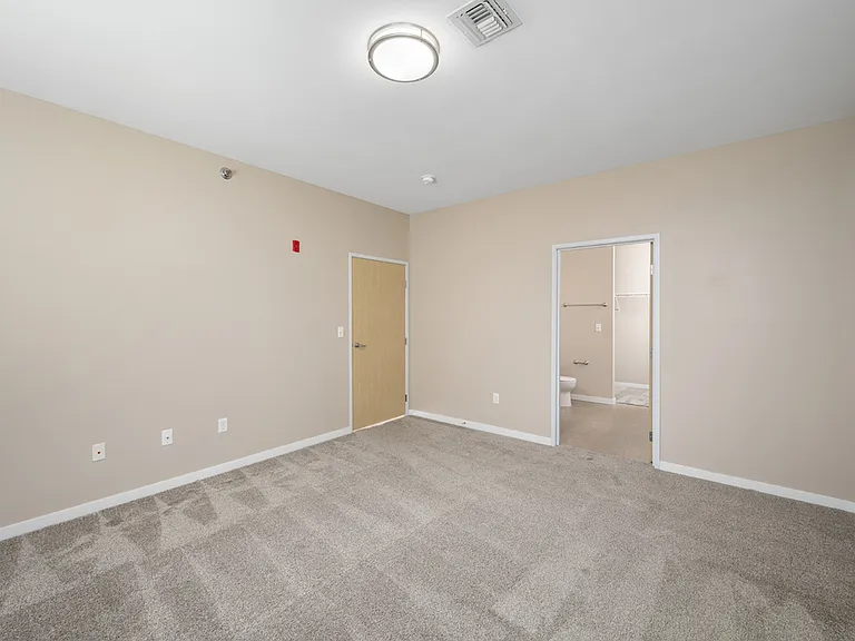 Bright and spacious bedroom with plush carpet, neutral walls, and an attached bathroom featuring a walk-in closet. Bright and spacious bedroom with plush carpet, neutral walls, and an attached bathroom featuring a walk-in closet.