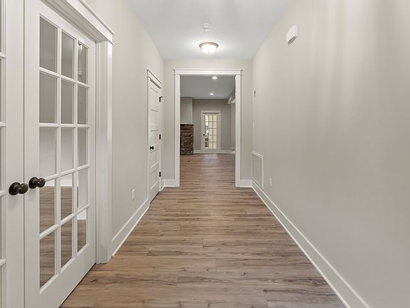 A hallway with wooden flooring and neutral walls. Glass-paned double doors are on the left, and a si