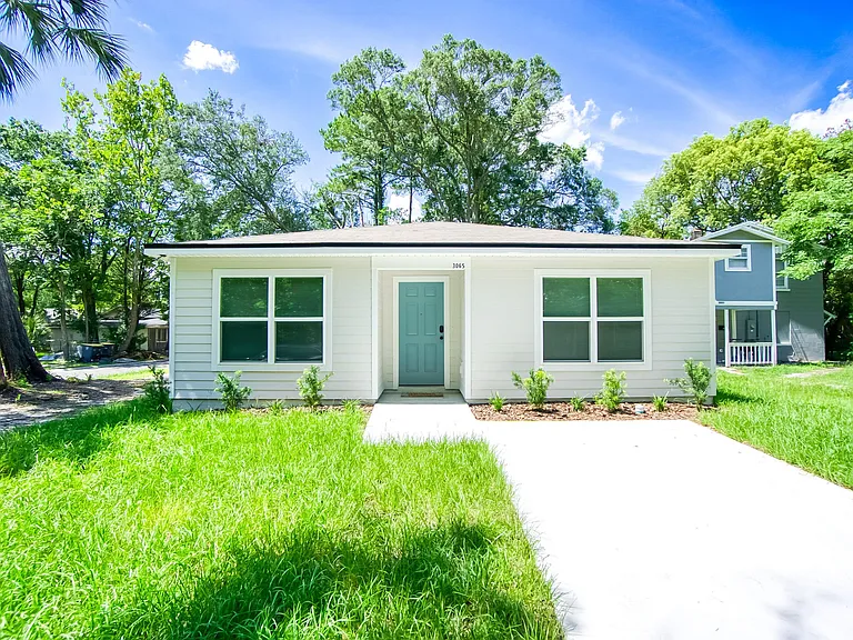 Single-story home with a covered entry, wide front walkway, and a spacious lawn framed by mature trees.