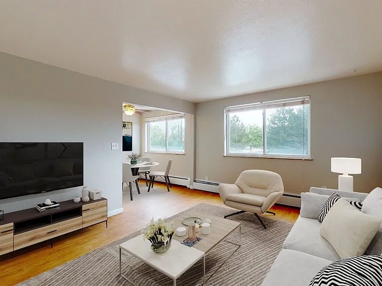 Bright open-plan living room with cozy seating, modern TV setup, and dining area, enhanced by large windows and stylish decor.