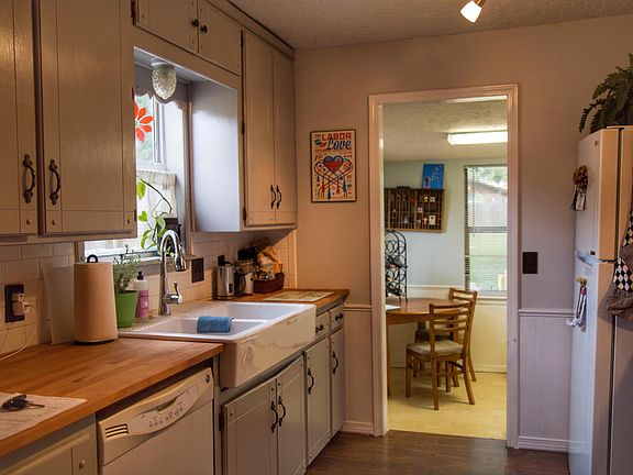 Vintage repainted kitchen has subway tile, farmhouse sink and laminate hardwood floors.