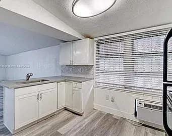 Eat-in kitchen area with ample cabinets, wide window with blinds, and durable flooring; includes a convenient in-room A/C uni