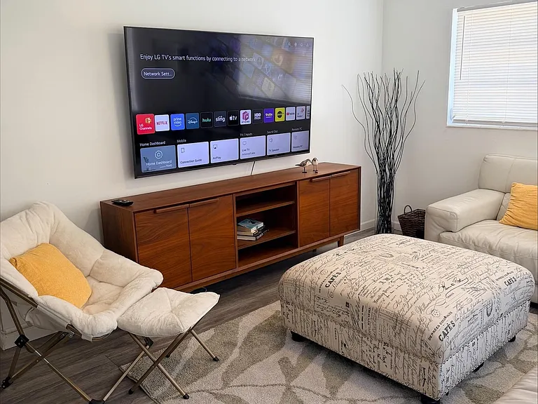 Comfortable living room with a mounted TV, ample seating, and an oversized ottoman for lounging or entertaining.