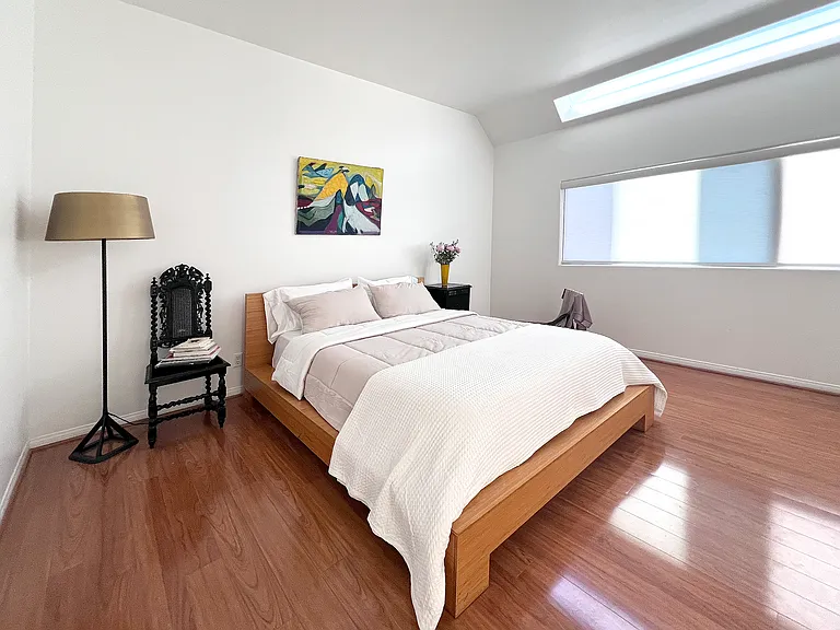 Spacious master bedroom suite featuring a clean minimalist design, high ceilings, and a modern skylight that floods the room with natural light.