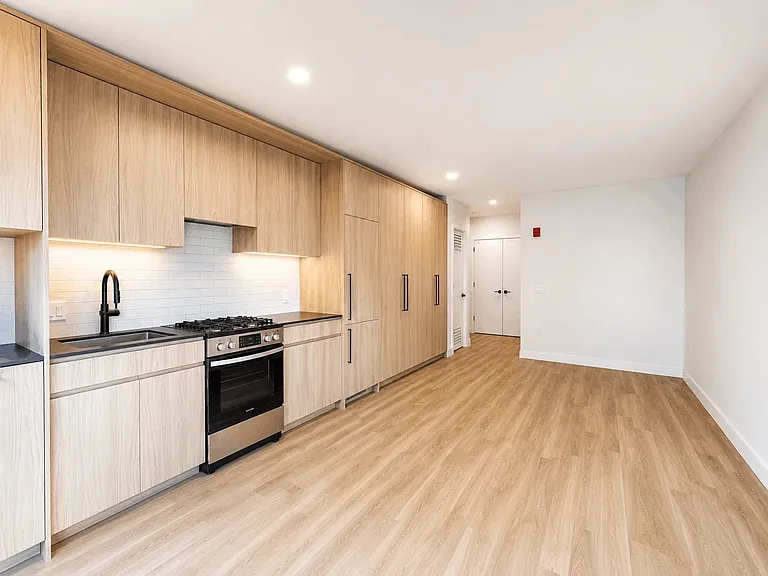 Modern studio kitchen at Stead 220 in Fulton Market featuring light wood cabinetry, a stainless steel gas range, white subway tile backsplash, and an integrated panel-front refrigerator and dish washer.