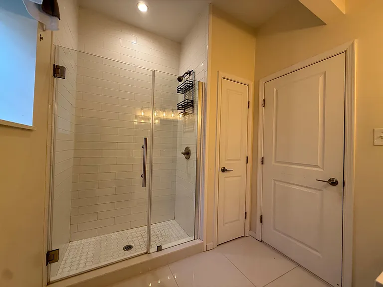 Glass-enclosed walk-in shower with subway tile surround and built-in storage, plus a clean tile floor and nearby linen/closet