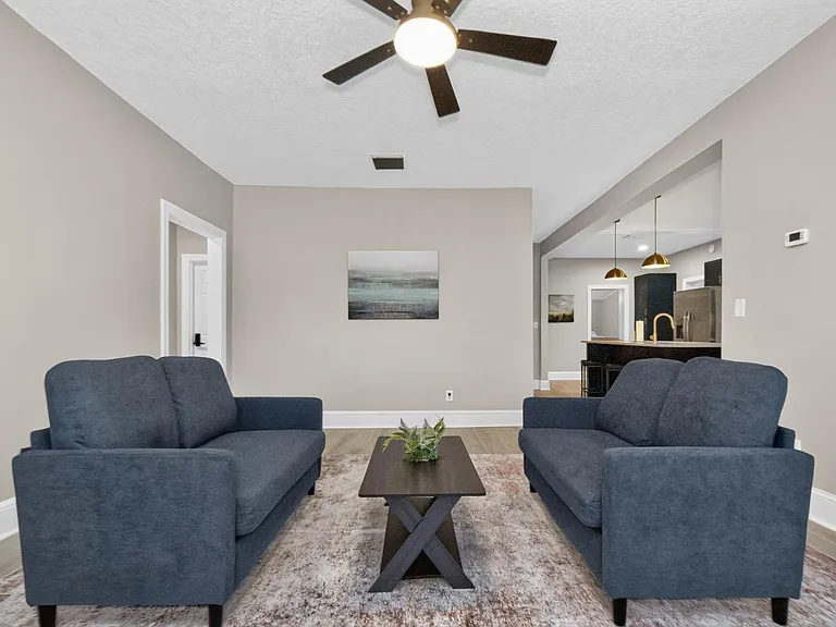 Open living area with two sofas, ceiling fan, and easy flow into the kitchen with a breakfast bar and pendant lighting.