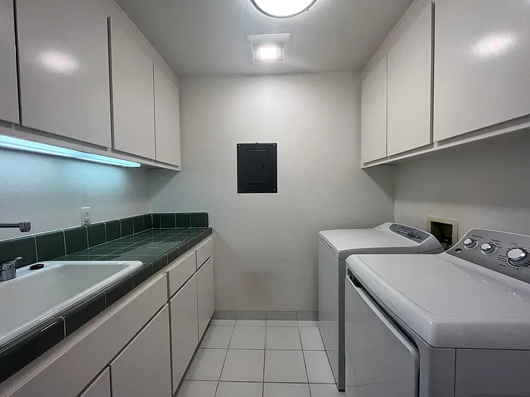 Convenient laundry room includes a utility sink, lengthy countertop and ample amount of storage cabinets.