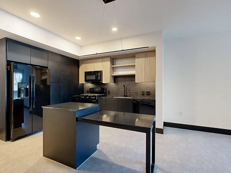Apartment kitchen with black appliances, dark counters, and tile floor.