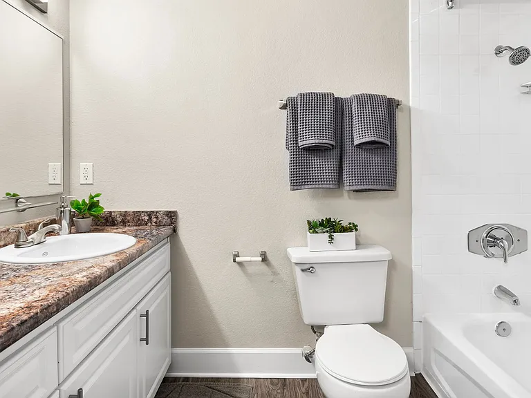 Step into our revitalized bathroom retreats, featuring deluxe granite-style countertops, grand wall-to-wall mirrors, and wood-style flooring with white tile surround for a luxurious and vibrant experience.