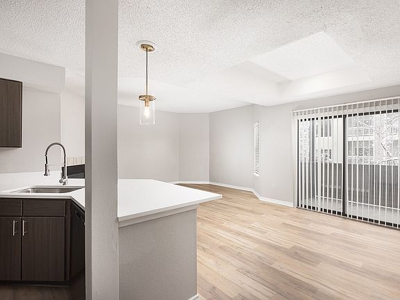 Modern apartment kitchen with elegant white countertops, stainless steel appliances, and warm wood flooring.