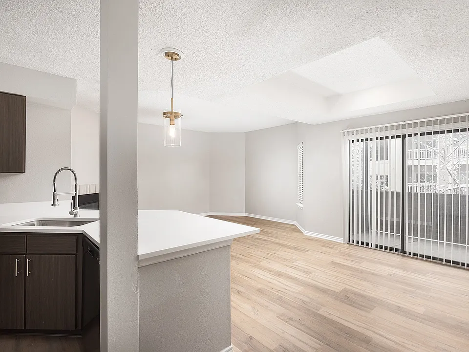 Modern apartment kitchen with elegant white countertops, stainless steel appliances, and warm wood flooring.