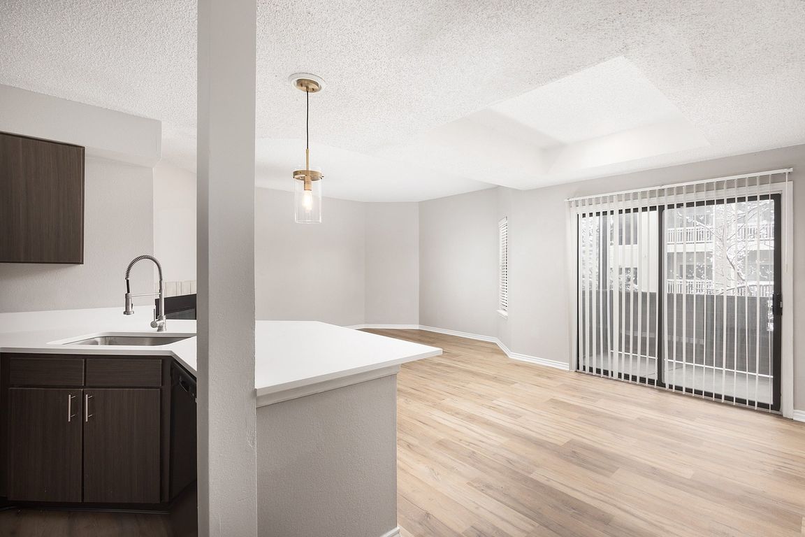 Modern apartment kitchen with elegant white countertops, stainless steel appliances, and warm wood flooring.