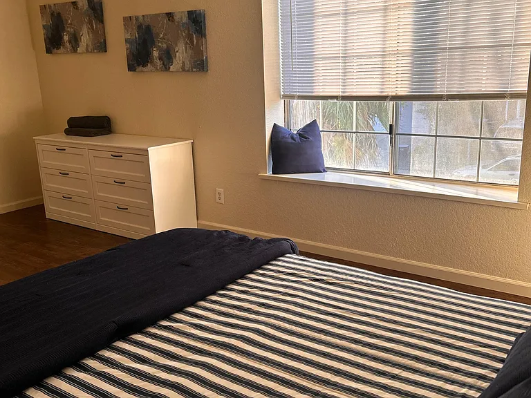 Well-kept bedroom with a large window and blinds, plus a dresser for convenient clothing storage.