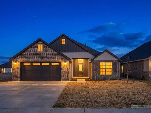 Single-story brick house with dark garage doors and warmly lit windows at dusk, set against a deep b