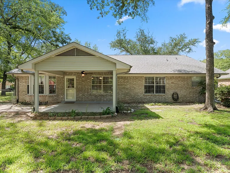 Brick exterior home featuring a covered patio, additional concrete patio area, and mature trees