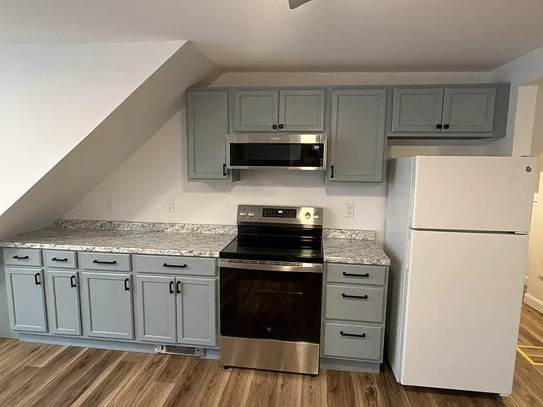 After stepping into the grand room, there is a refrigerator and a brand new stove (installed 12 May 26). Above the stove is microwave that is a light for the stove and an exhaust fan and a microwave. installed on Tuesday, 12 May.