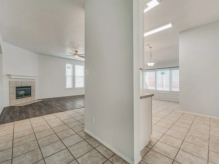 Tiled flooring entryway opening to a living area with a fireplace featuring a tile surround and mantel