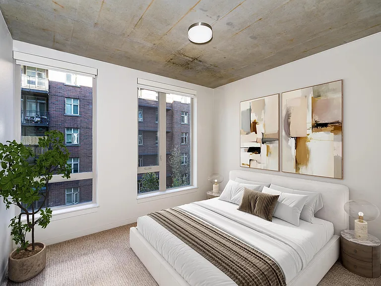 A flexible bedroom with concrete ceilings, soft carpeting, and natural light, offering a versatile space that adapts to work, rest, or creativity.