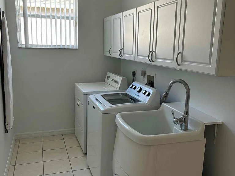 Laundry room fully equipped with a new washer, dryer, utility sink, and storage cabinets