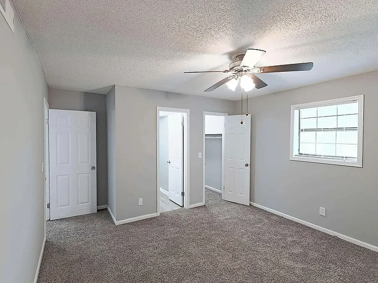 Spacious bedroom with plush carpeting, ceiling fan, and natural light