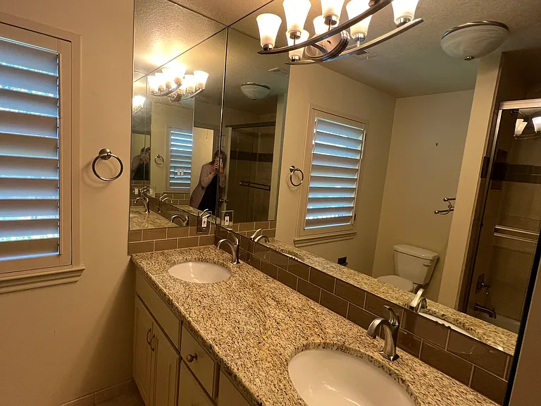 Hall bath with two sinks, tile surround in tub, glass shower doors. Shutters have the top adjustable for viewing outside but still offer privacy.