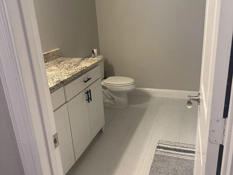 Full bath with a granite-top vanity, storage cabinet, and tile flooring for easy upkeep.
