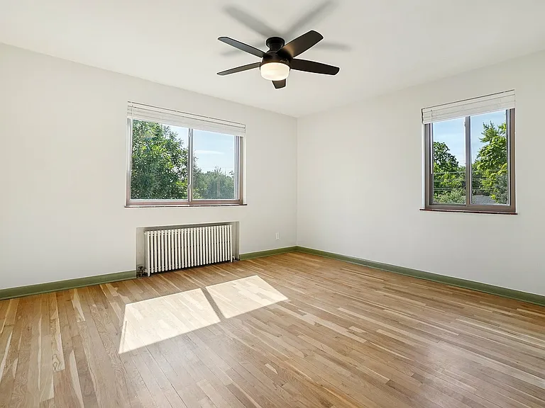 Bright and airy bedroom with elegant wood flooring, stylish ceiling fan, and large windows with garden views.