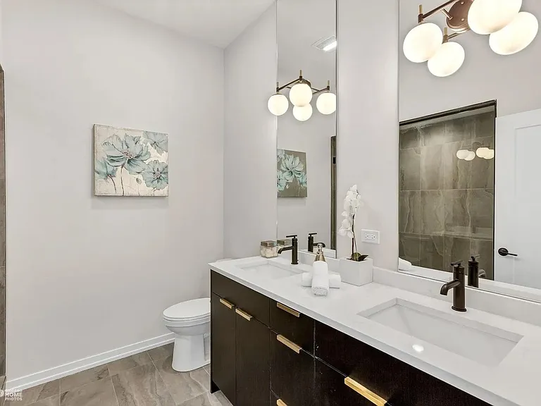 Primary Bathroom: Spa-like primary bath with double quartz vanity, dark cabinetry with gold hardware, frameless glass shower, and statement globe lighting