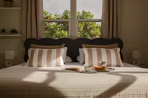 Inviting bedroom with a queen-sized bed and soft linens. Sunlight fills the room, and bedside lamps add warmth and a stylish, relaxed vibe.