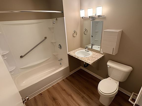 Elegant bathroom with wood flooring, featuring a modern bathtub, granite countertop vanity, and sleek lighting. Elegant bathroom with wood flooring, featuring a modern bathtub, granite countertop vanity, and sleek lighting.