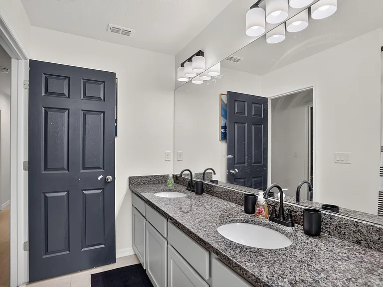Bathroom features a long double-sink vanity with granite-style counters, ample storage, and a large wall mirror.