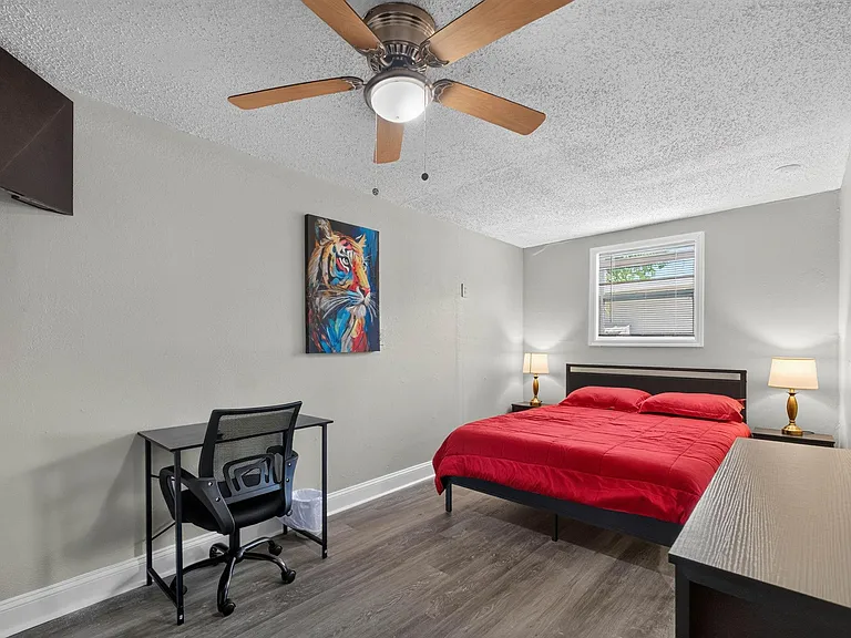 Furnished bedroom with a full bed, desk workspace, ceiling fan, and a window with blinds for natural light.