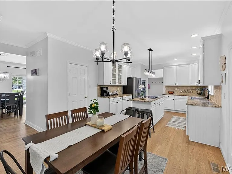 Open-concept dining area featuring a dark wood-finish table, wood-finish flooring, and a contemporary chandelier