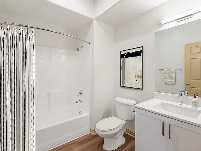 Renovated Package I bath with white speckled quartz countertop, white cabinetry, and hard surface flooring