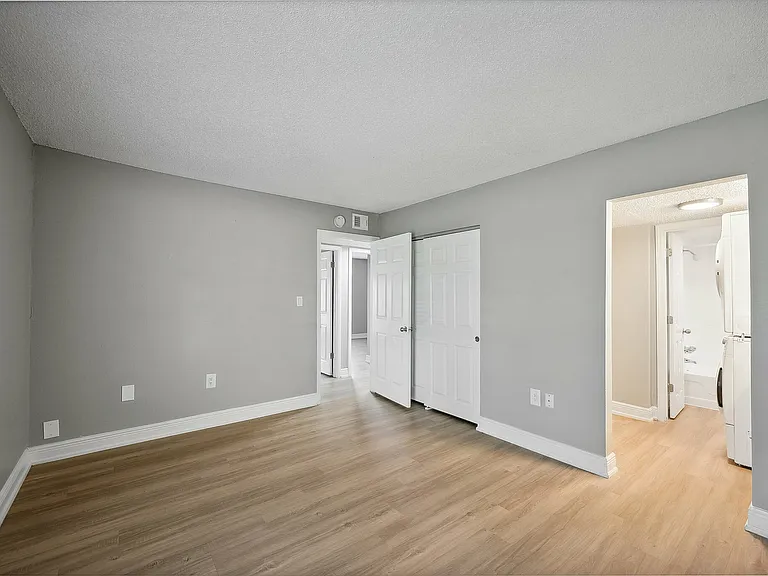Inviting bedroom with elegant gray walls and rich wood flooring, featuring a doorway leading to a modern bathroom and in-unit laundry area.