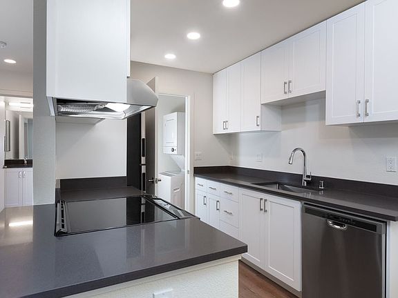 Kitchen with white cabinetry, stainless steel appliances, dark grey countertops and hard surface flooring