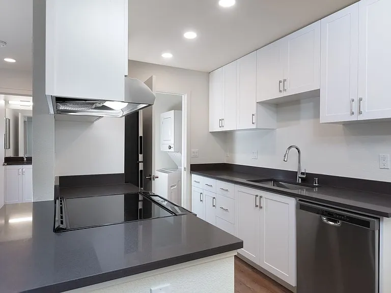 Kitchen with white cabinetry, stainless steel appliances, dark grey countertops and hard surface flooring