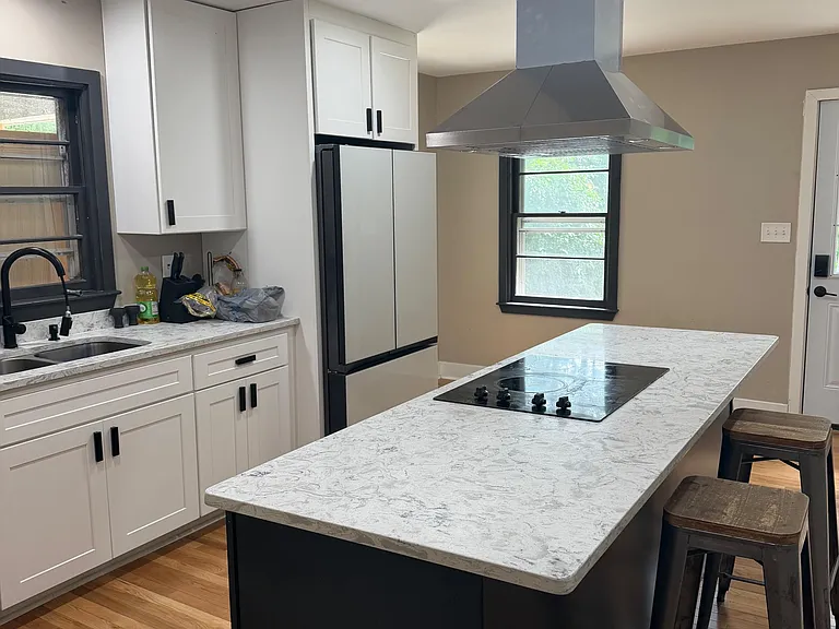 Updated kitchen with shaker cabinets, stone-look counters, center island cooktop, and vent hood plus bar seating.