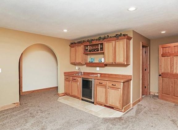 Lower level wet bar. With butcher block countertops and truffle marble tile. Wine fridge stays with the home. Custom Cherry cabinets.  And arched hallway leading to the lower level master bedroom/bath and exercise room.