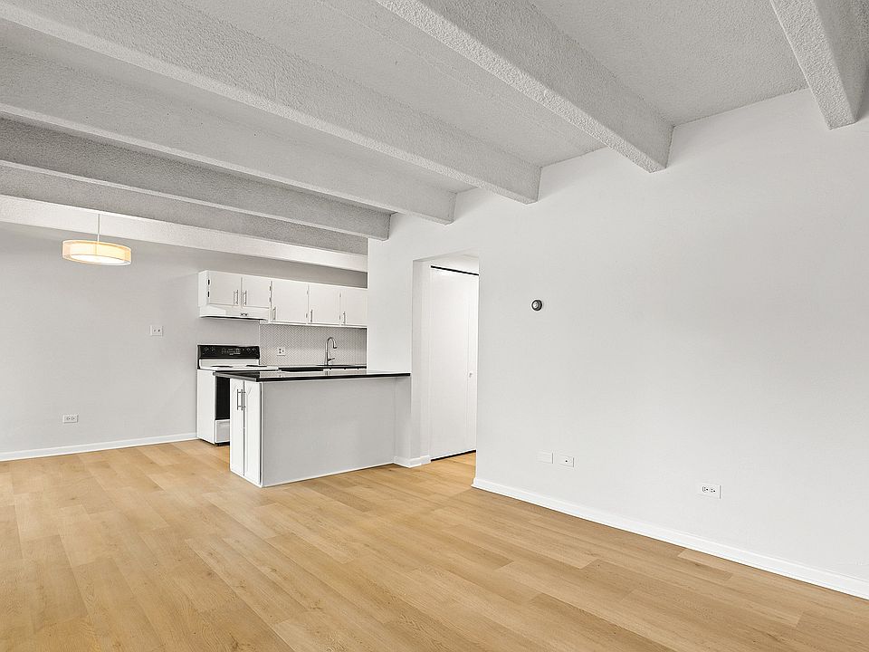 Elegant open-plan space with light wood flooring and modern kitchen featuring sleek countertops and white cabinetry.