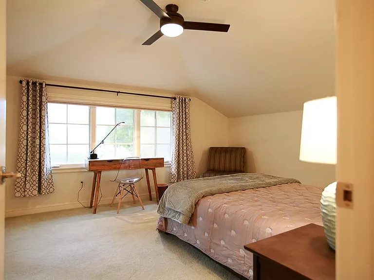Upstairs bedroom #1 vantage point from the entrance facing the desk office area with a large picture window plus blackout curtains and a corner reading chair off to the side.